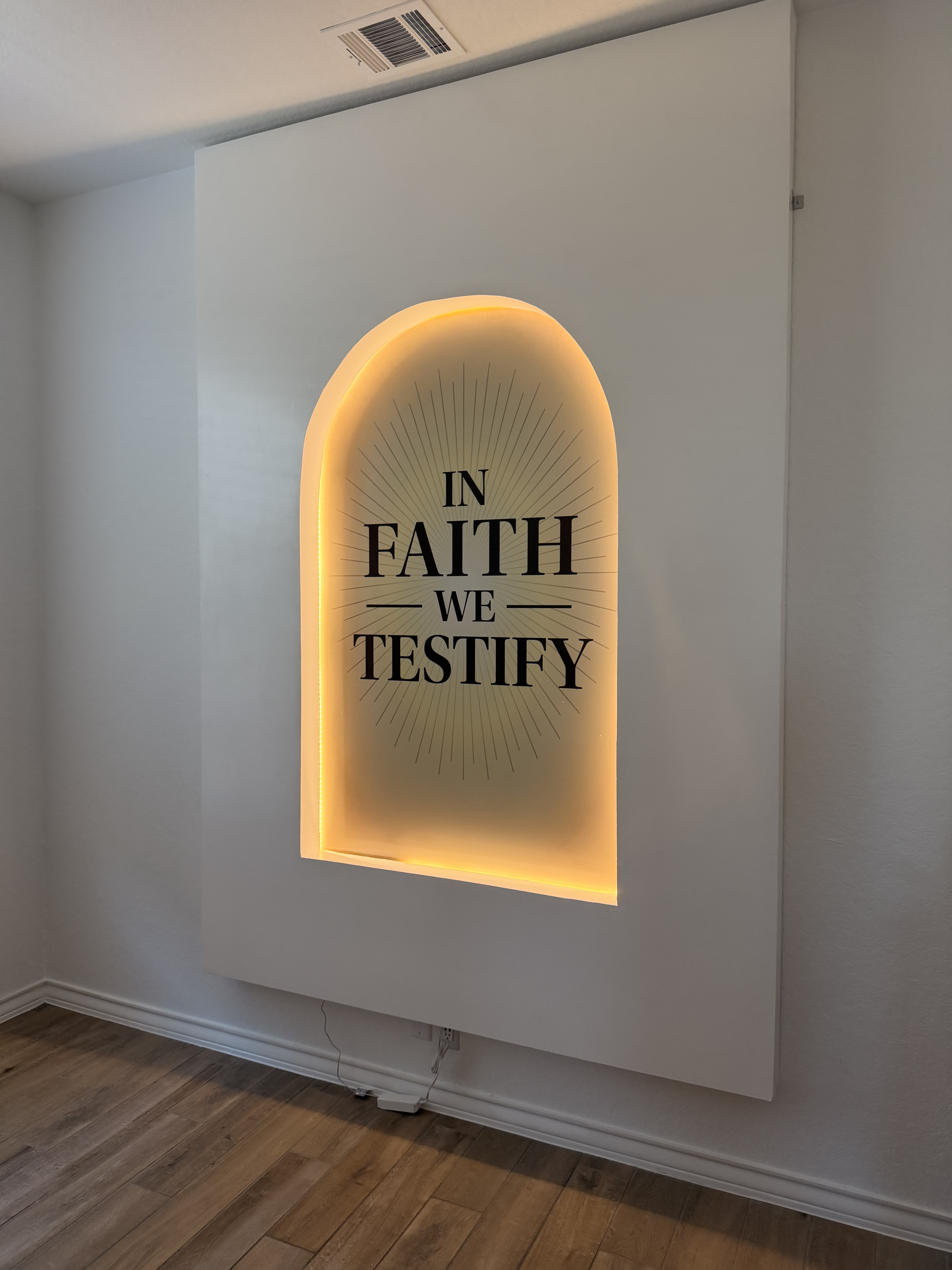 The branded 'In Faith We Testify' arch with warm golden backlight — the podcast studio